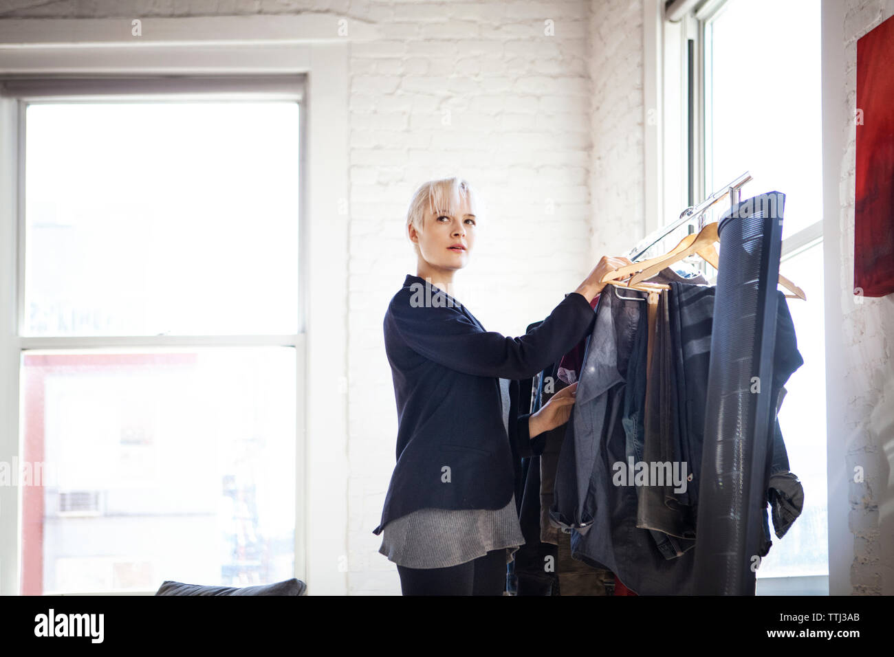Thoughtful woman choosing clothes from rack at home Stock Photo
