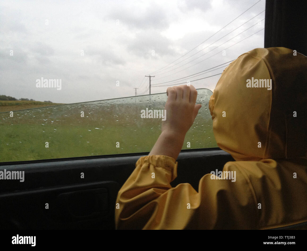 Rear view of boy looking through car window during rainy season Stock Photo