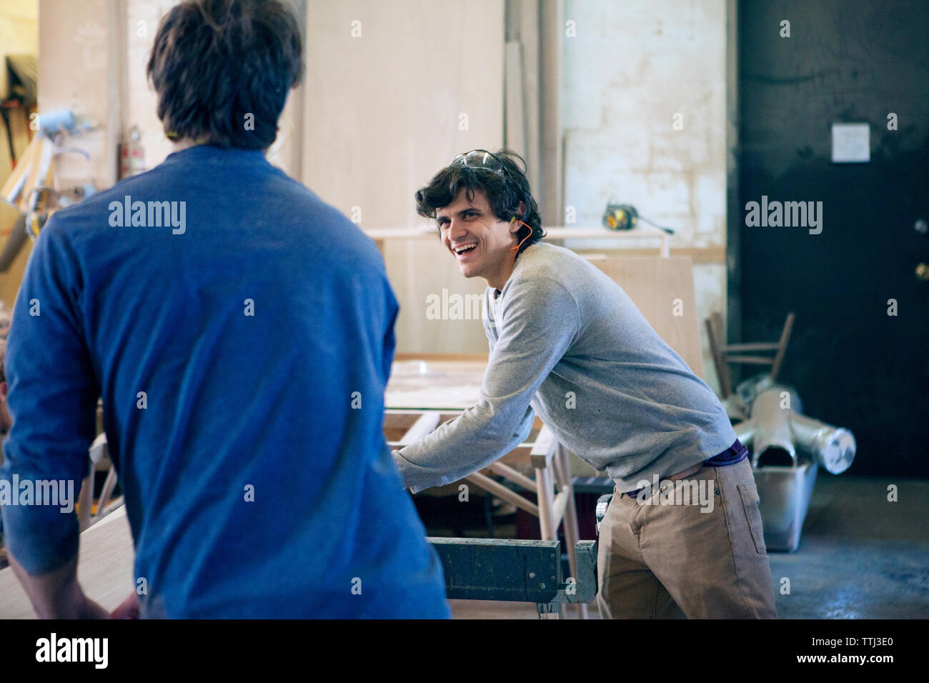 Happy carpenter talking to colleague while working in workshop Stock Photo