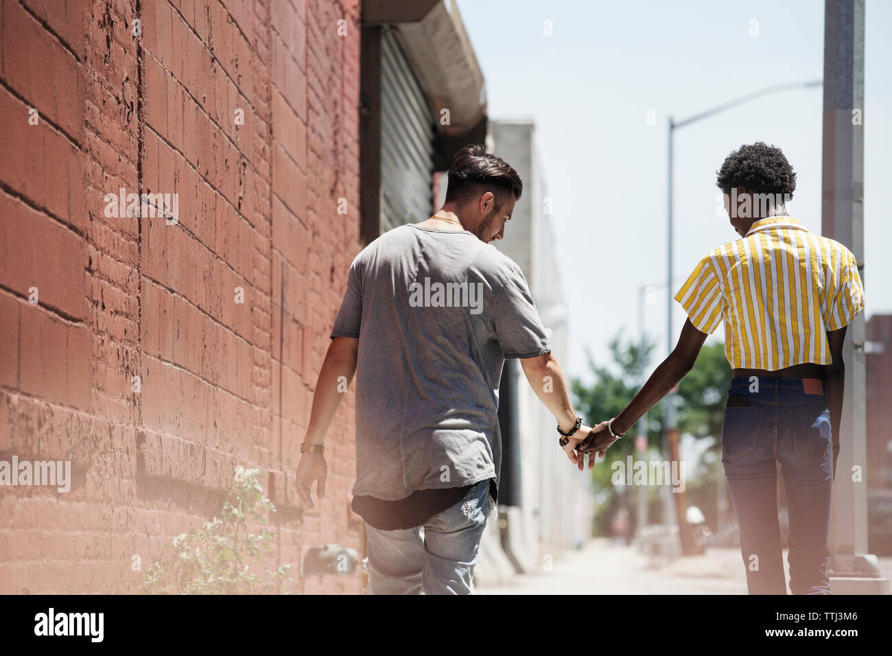 Rear view of couple holding hands while walking on sidewalk Stock Photo ...