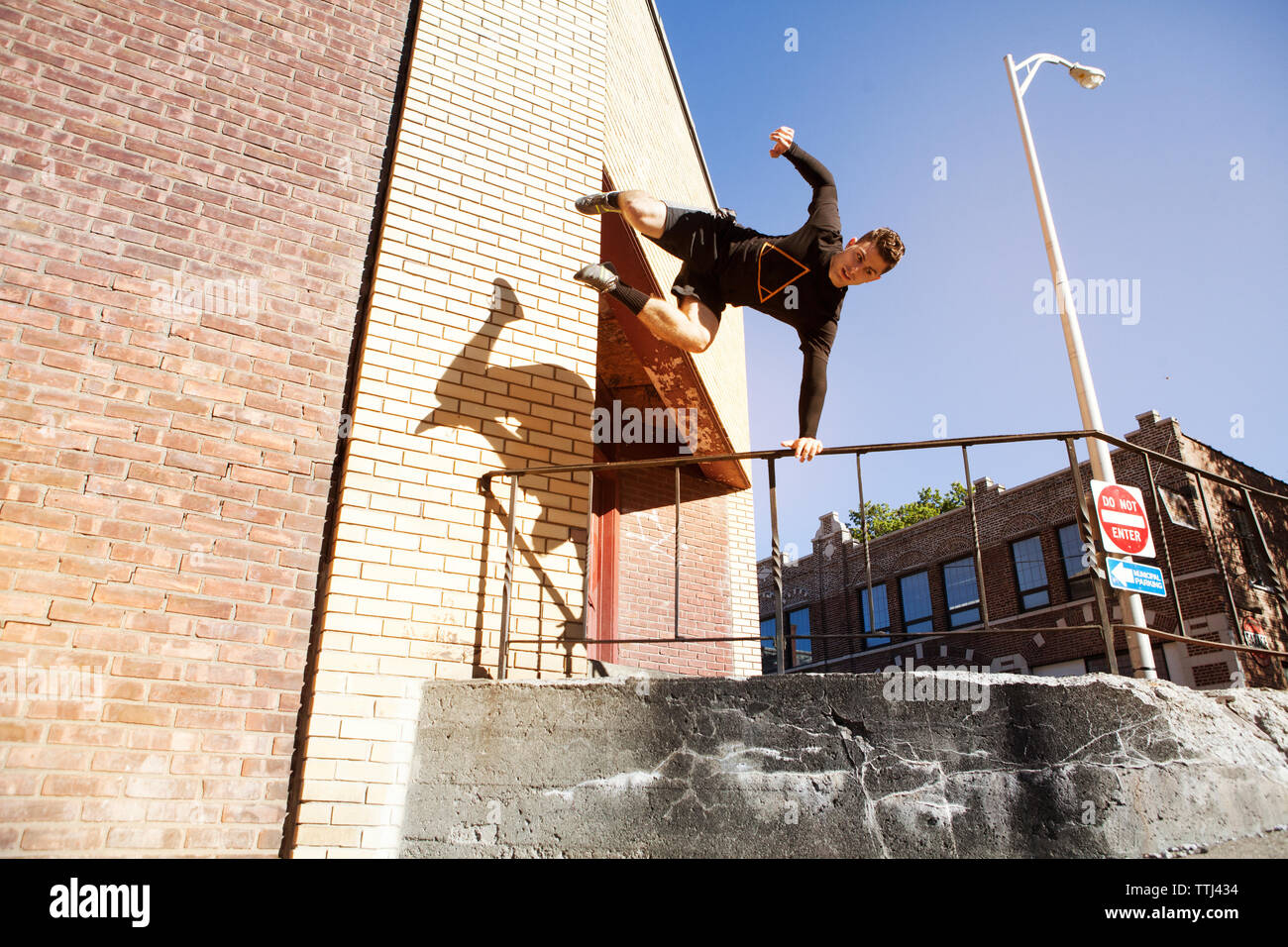 Low angle view of confident man jumping over railing against clear blue