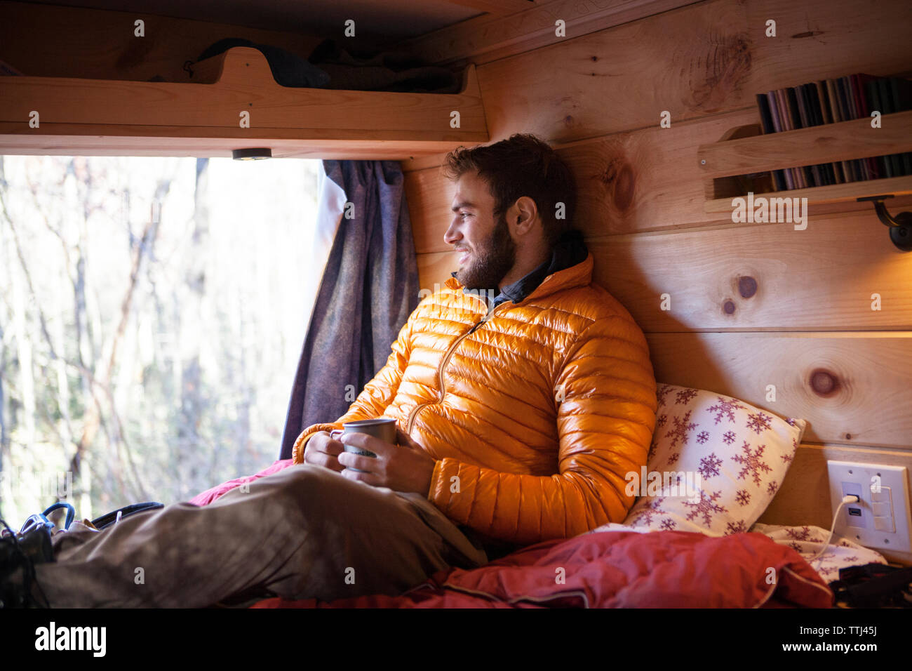 Smiling man with mug looking away while sitting on bed in camper van Stock Photo