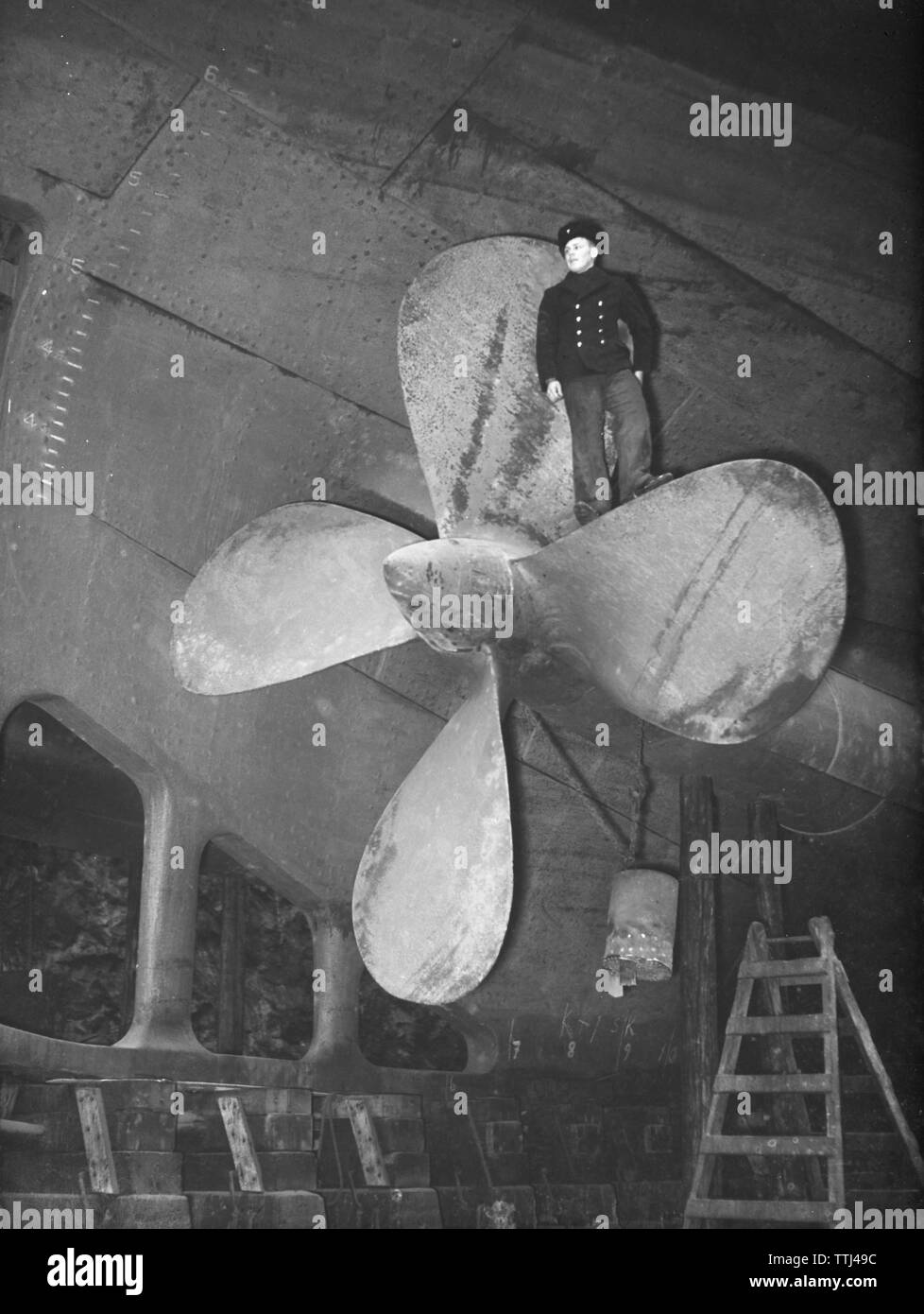 Dockyard in the 1940s. The icebreaker Ymer is being serviced at a wharf and a man is standing on the stern propeller. Sweden 1941. Kristoffersson ref 172-8 Stock Photo