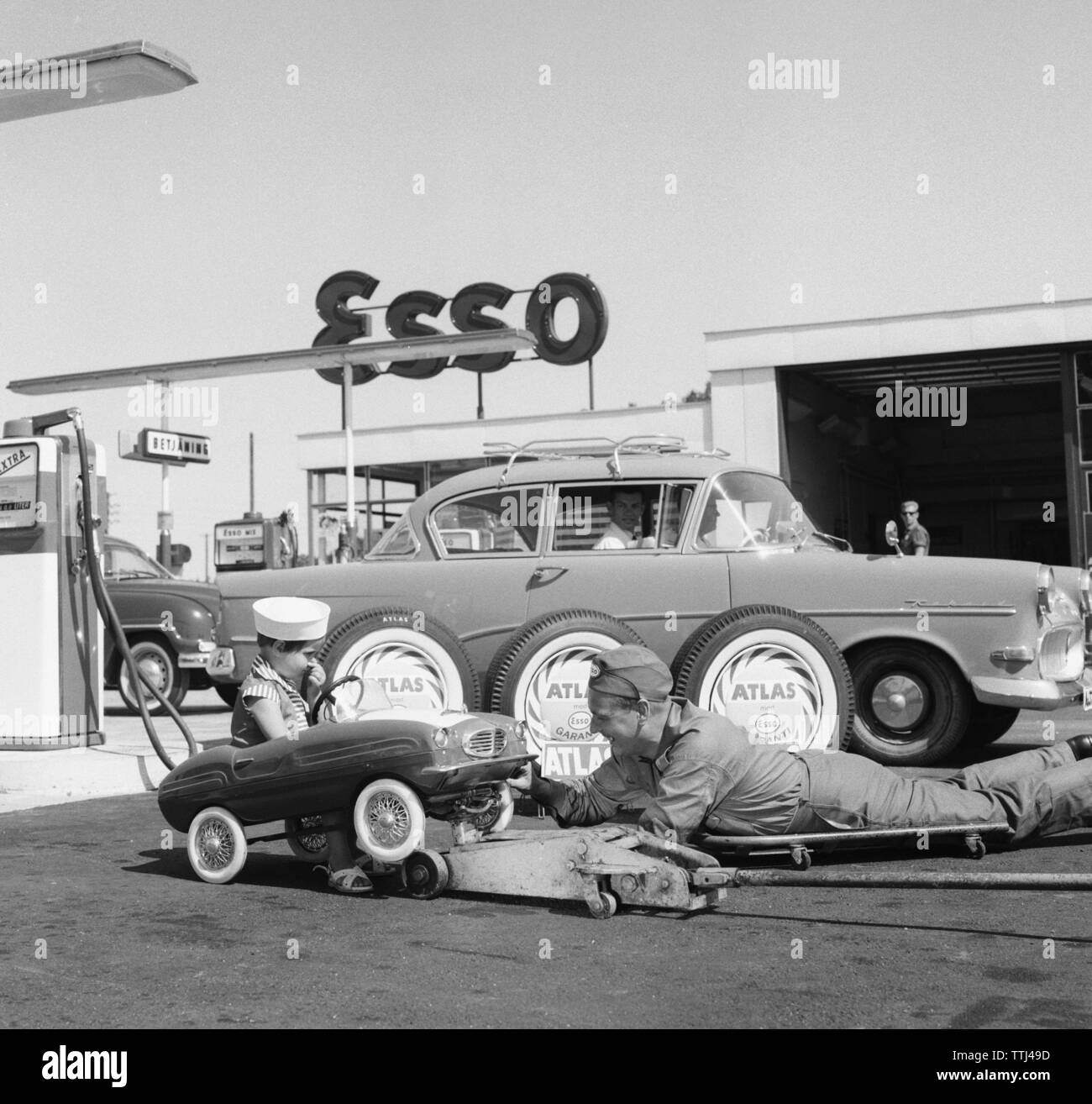 Service station of the 1950s. A boy in his pedal car has it serviced at an Esso petrol station. A service man has lifted the small car up and is servicing it.  Sweden 1958. Kristoffersson ref DC100-9 Stock Photo