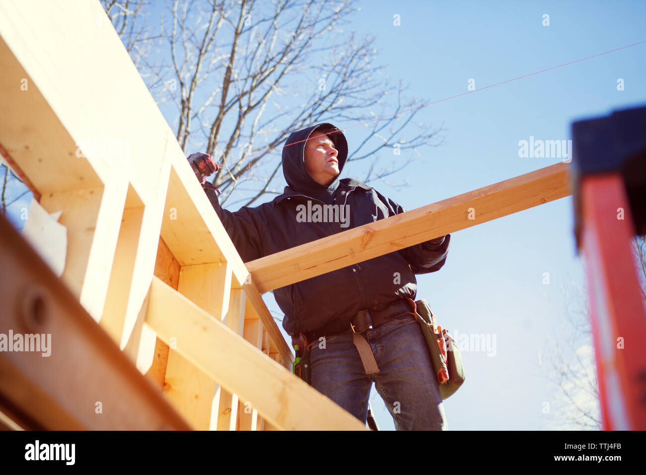 Low angle view of worker constructing wooden house against blue sky Stock Photo