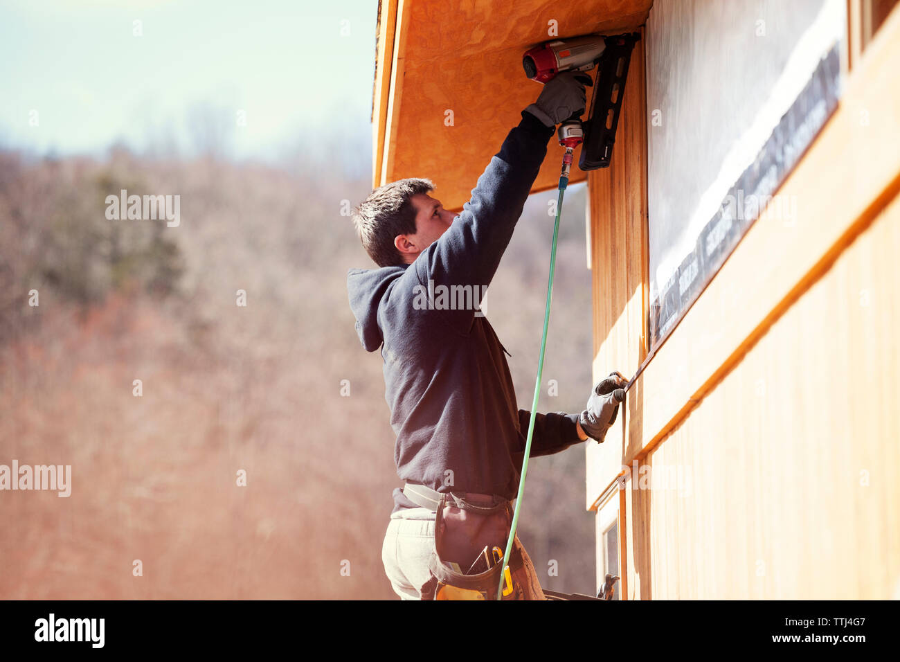Worker using drill machine while constructing house during sunny day Stock Photo