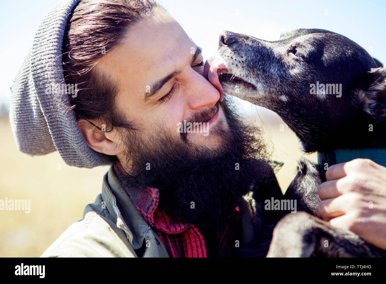 Close-up of dog licking man's face during sunny day Stock Photo