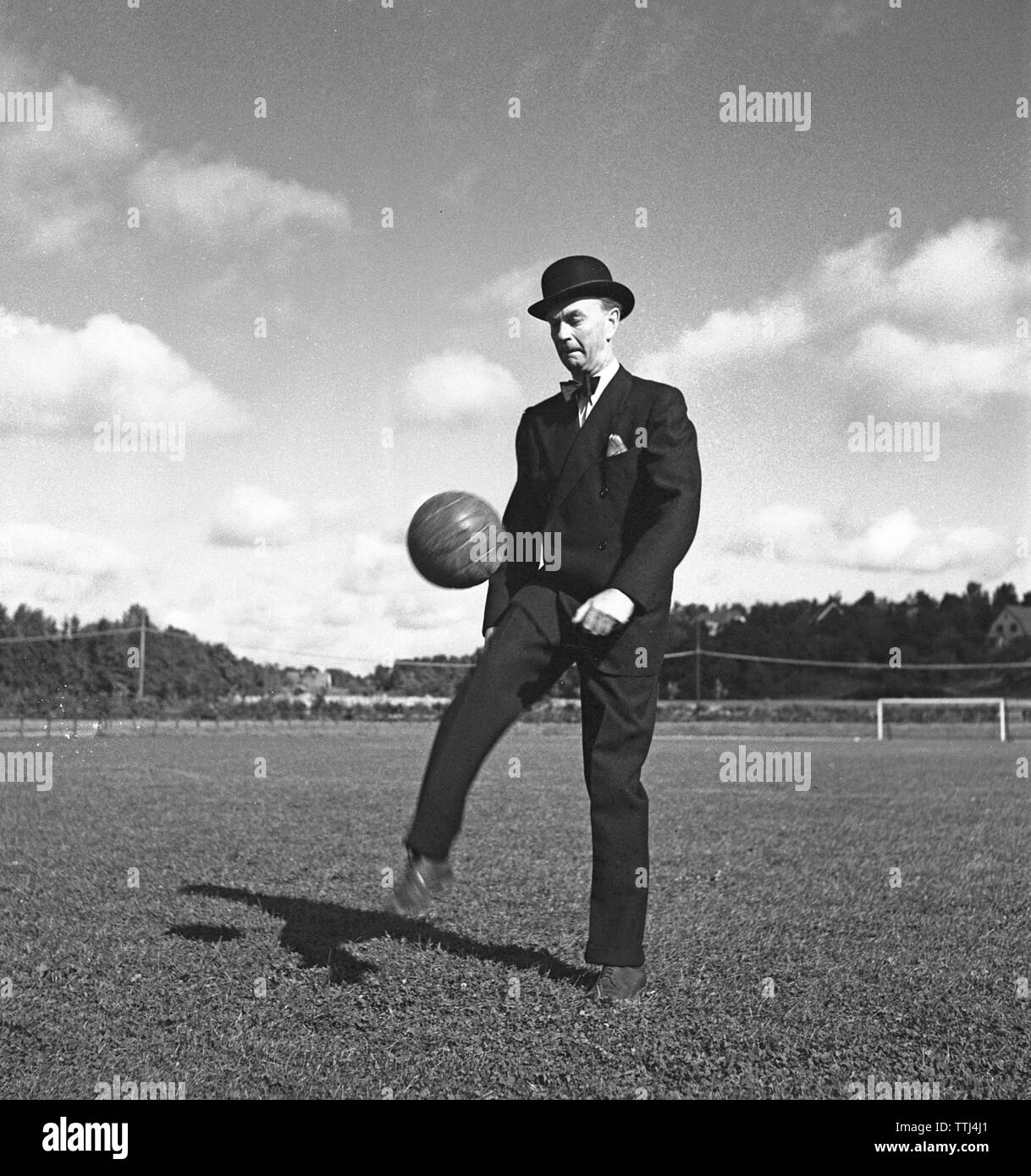 1940s soccer player. A gentleman dressed in a suit and a bowler hat is kicking a football in the air. Sweden 1944 Kristoffersson F104-1 Stock Photo