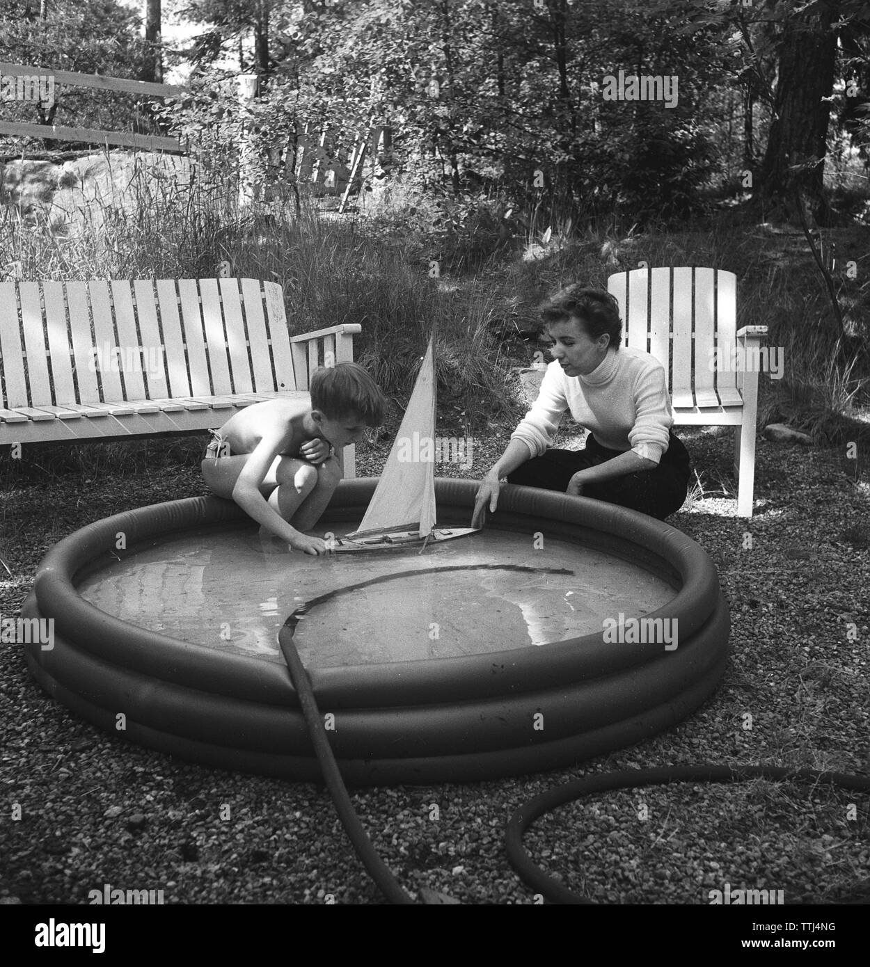 Playing in the 1950s. A mother and son on a summer's day. The boy is playing with a model sailing boat and puts it in the water. Sweden 1954  Kristoffersson ref BP35-2 Stock Photo