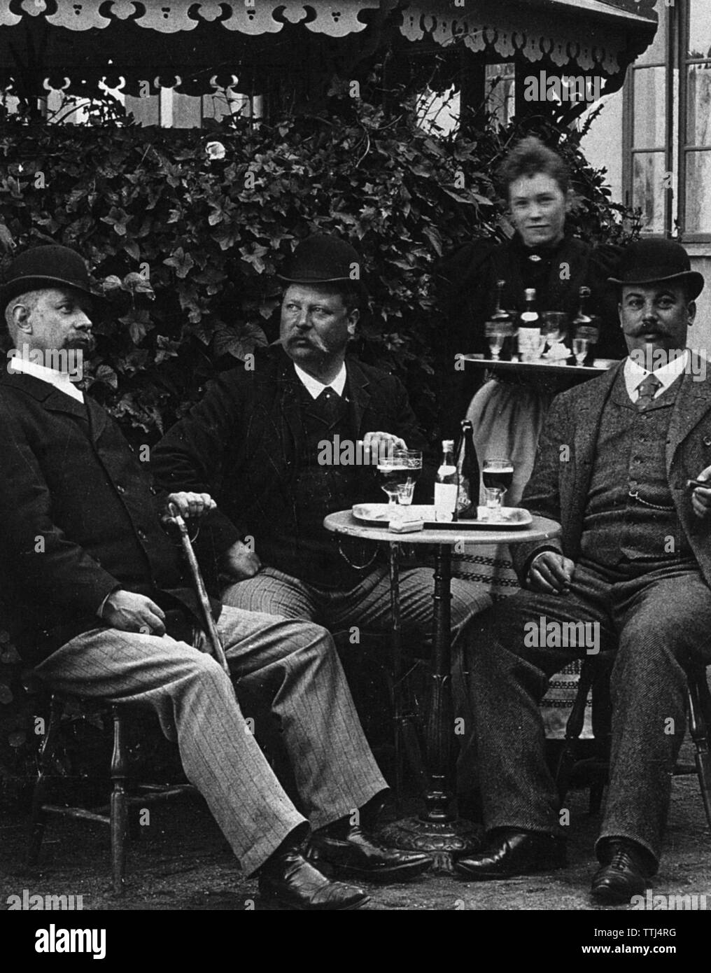 Men's lifestyle in the beginning of the 20th century. Three men are sitting at a table at a restaurant enjoying a glass of beer. They are all three typically well dressed and hats are on.  Sweden 1800-1900 BV67-3 Stock Photo