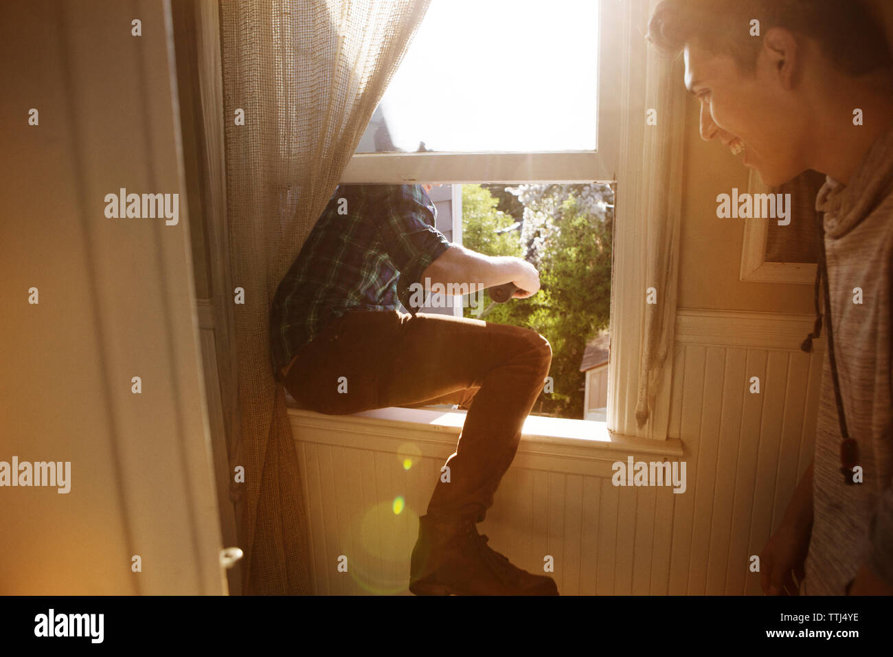 Man looking at friend sitting on window at home Stock Photo