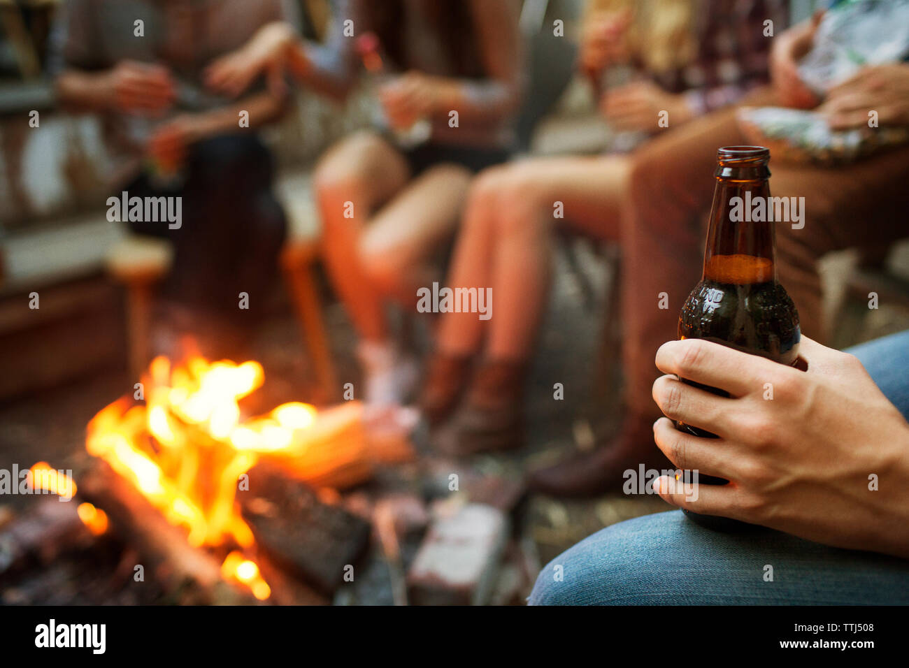 Cropped image of man holding beer bottle while camping with friends Stock Photo