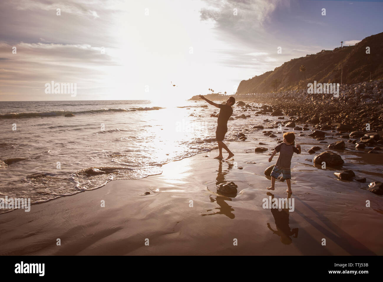 Father and son throwing stones in sea during sunset Stock Photo