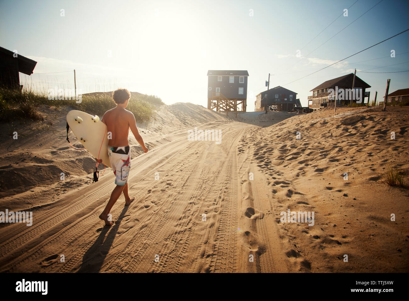 Rear view of man holding surfboard walking on sand at beach Stock Photo ...