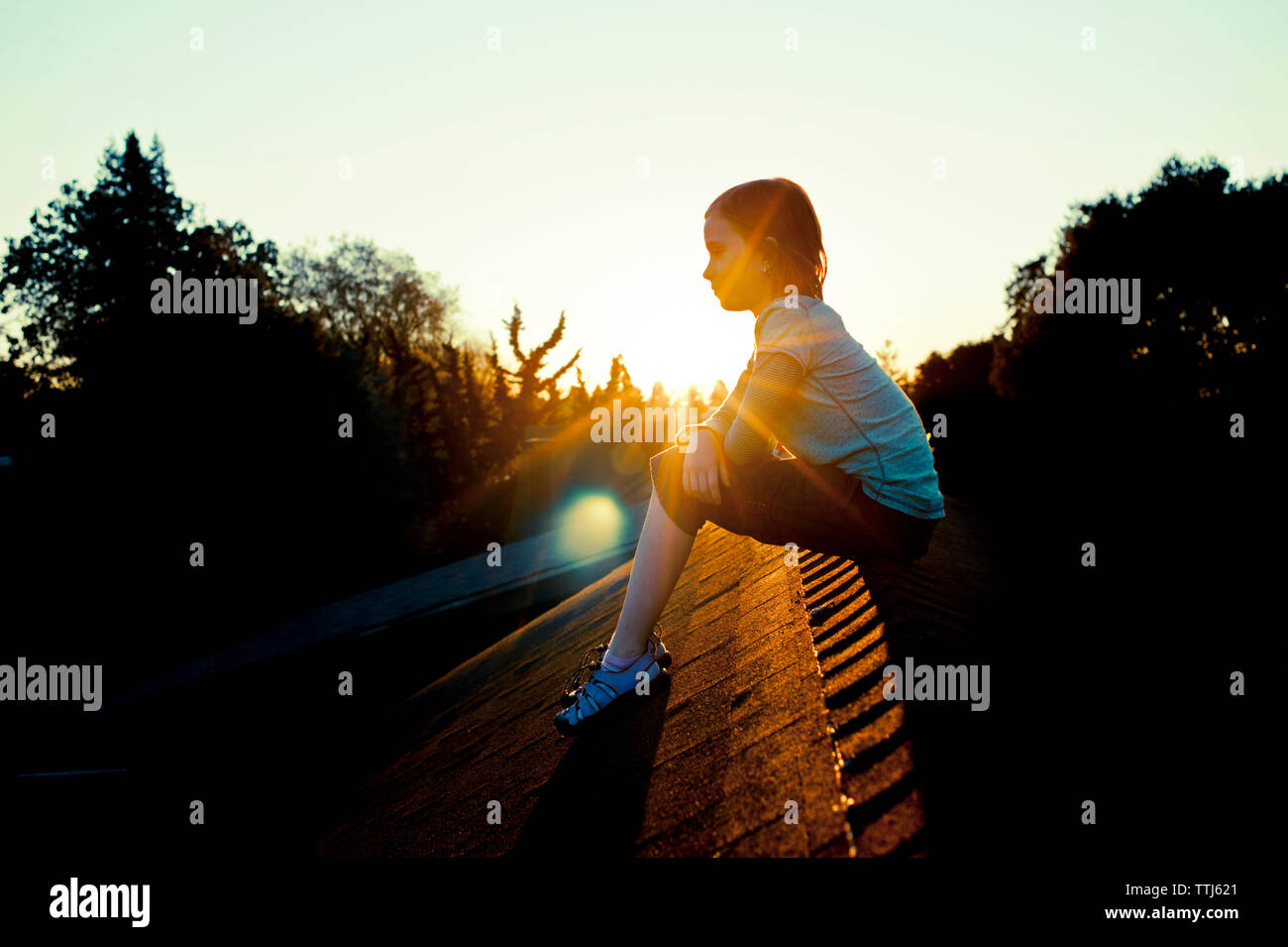 Side view of girl sitting on roof against clear sky Stock Photo - Alamy