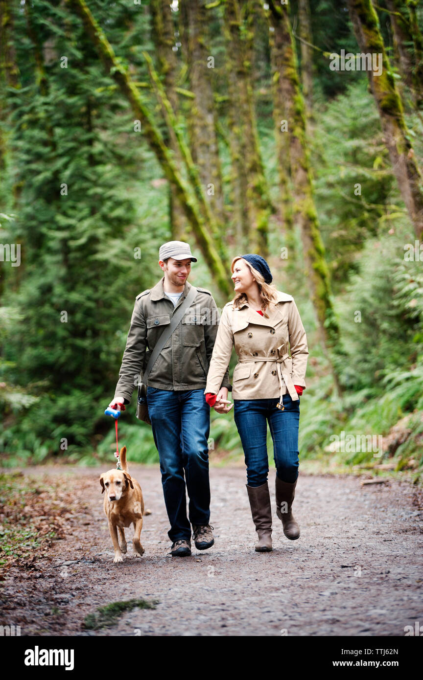 Couple holding hands while walking on road in forest Stock Photo - Alamy