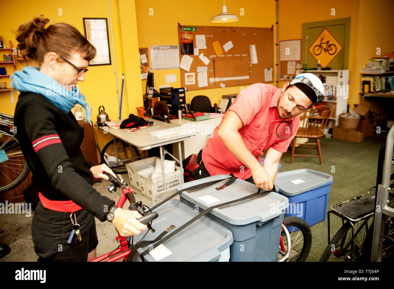 Man and woman tying containers on bicycle at workshop Stock Photo