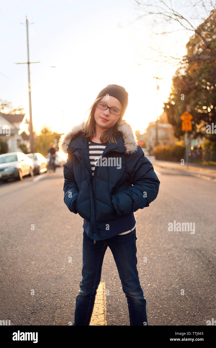 Portrait of girl with hands in pockets standing on road against sky ...