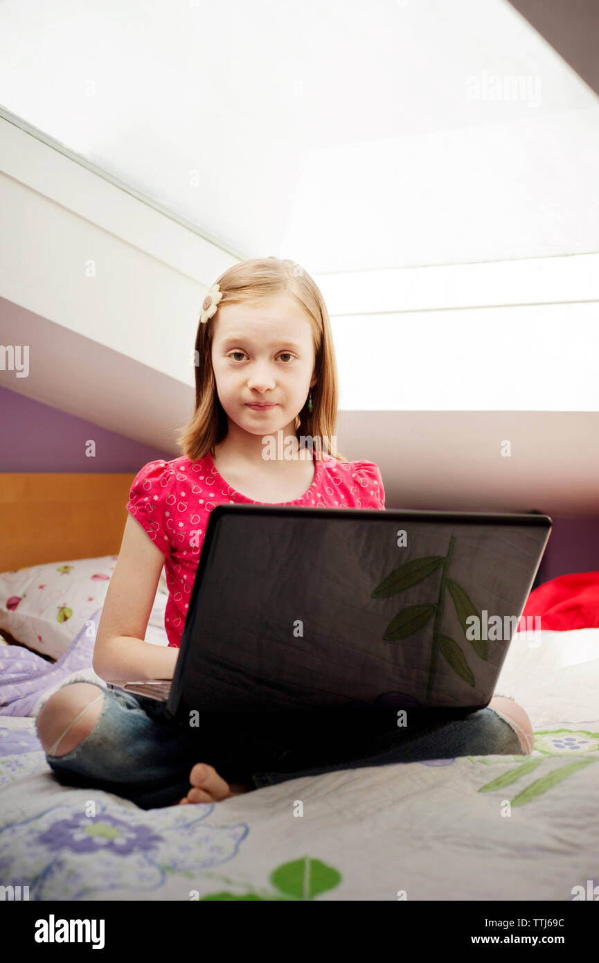 Portrait of girl sitting with laptop computer on bed at home Stock