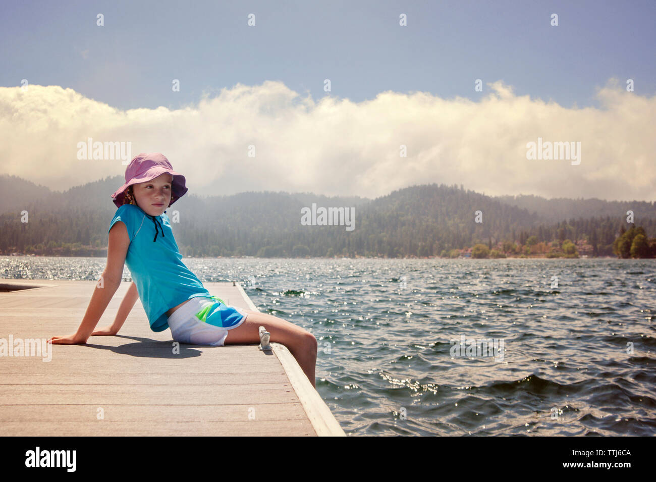 Girl looking away while sitting on pier at lake Stock Photo - Alamy