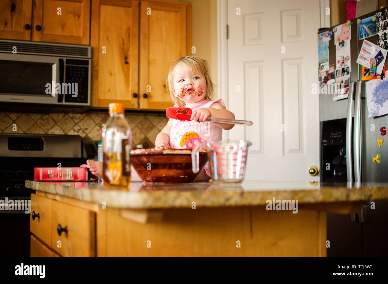 Girl eating chocolate while sitting on kitchen island Stock Photo