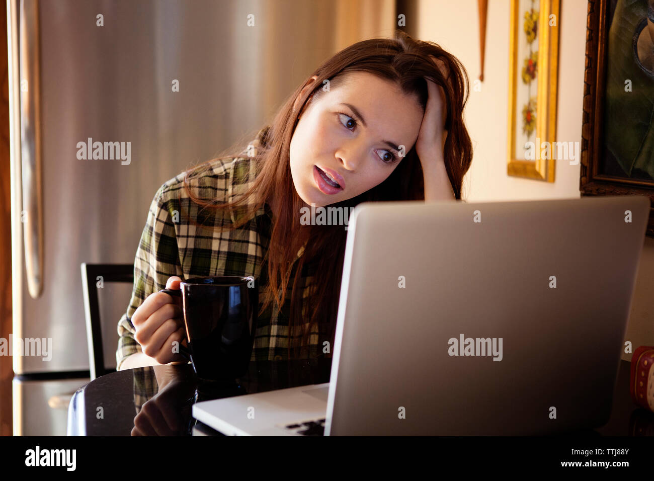 Woman coffee mug looking at laptop computer while sitting at home Stock Photo