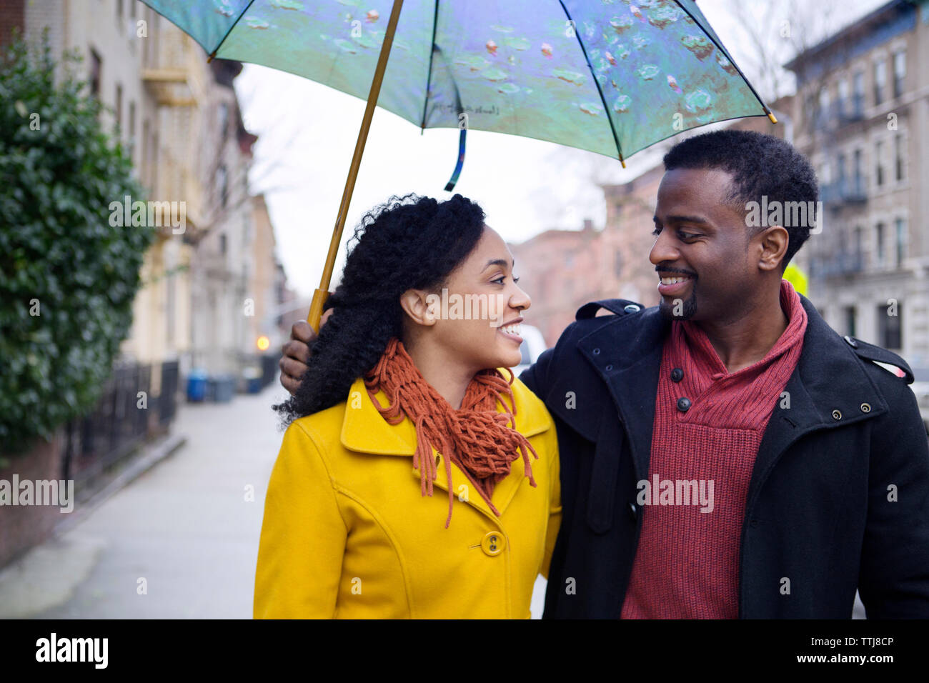 Man holding umbrella while walking with woman on road in city Stock Photo