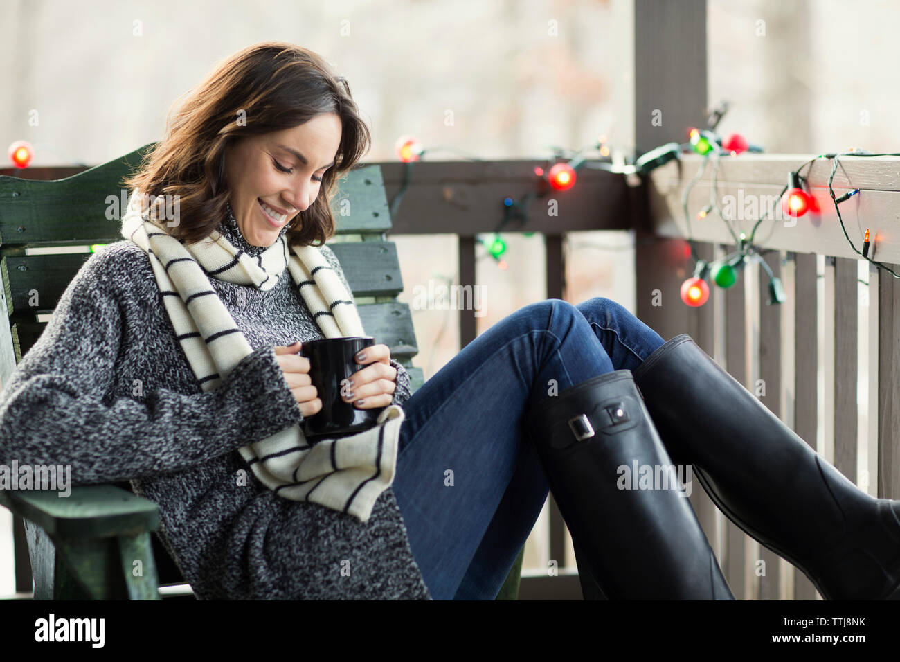 Woman smiling while sitting on wooden chair in porch Stock Photo - Alamy