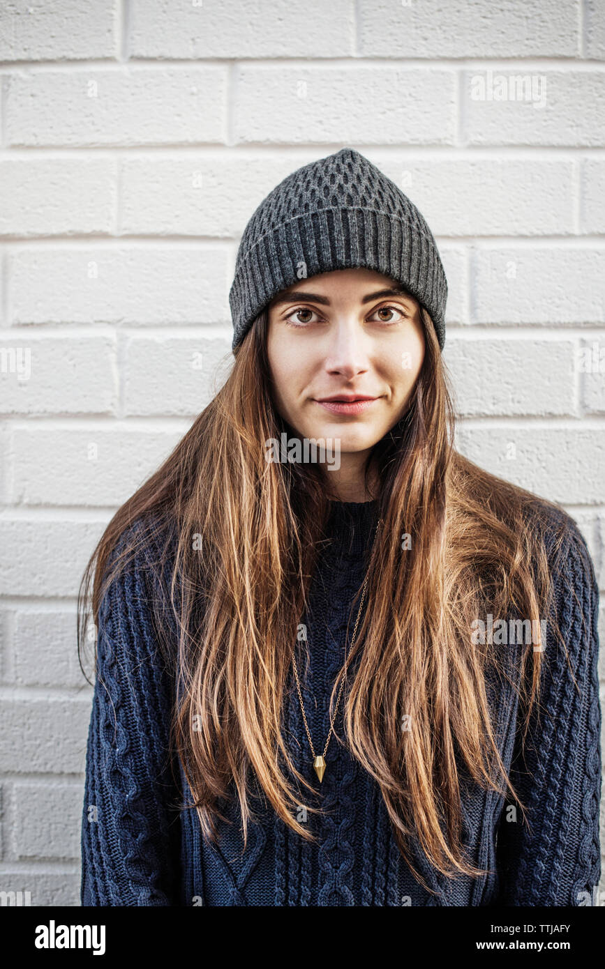 Portrait of woman wearing knit hat standing against brick wall Stock Photo