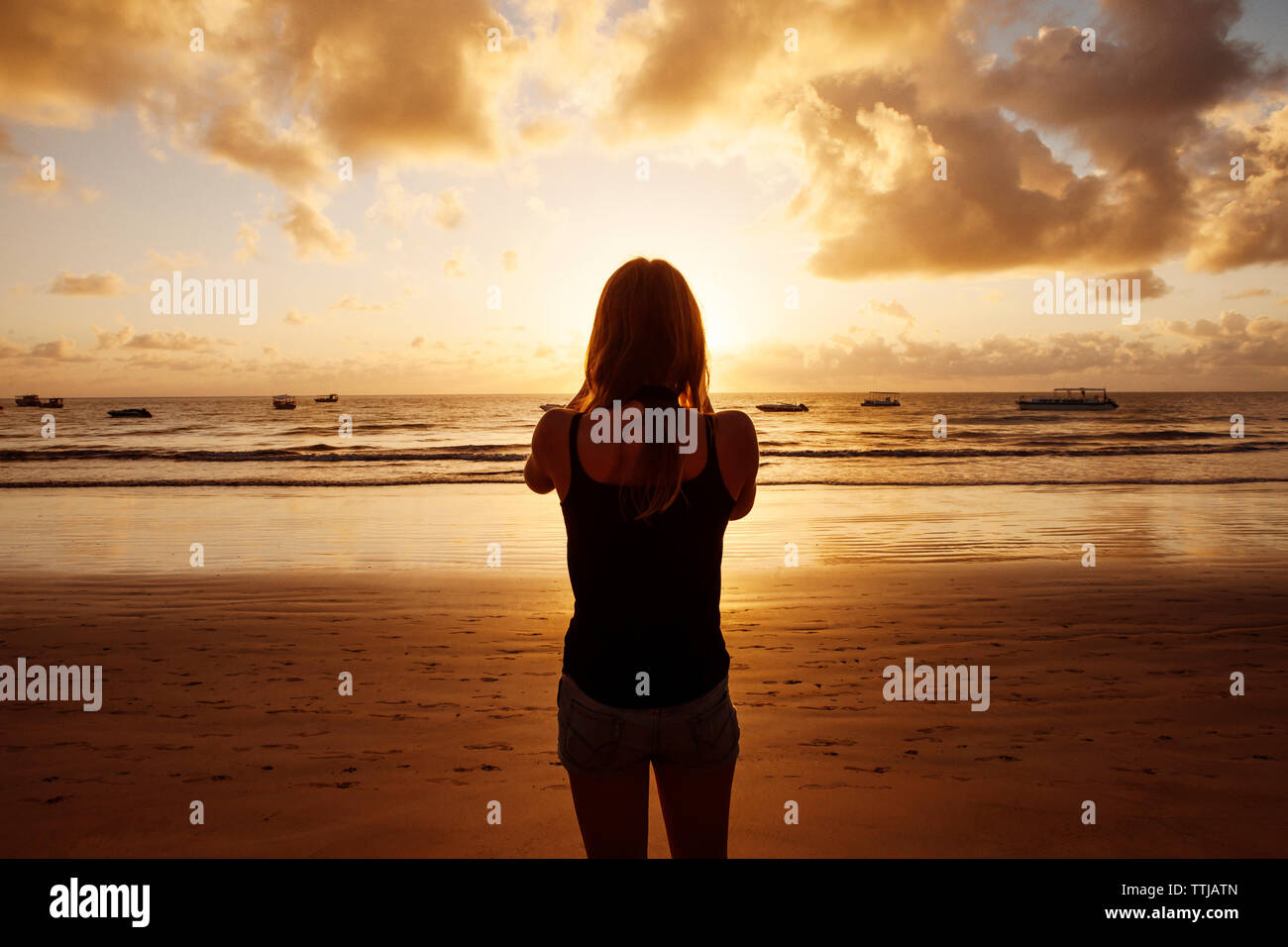 Rear view of woman standing at beach during sunset Stock Photo - Alamy