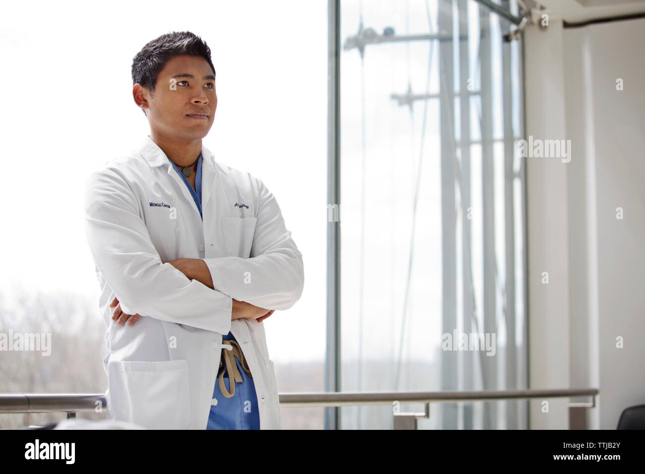 Man with arms crossed standing against window in hospital Stock Photo
