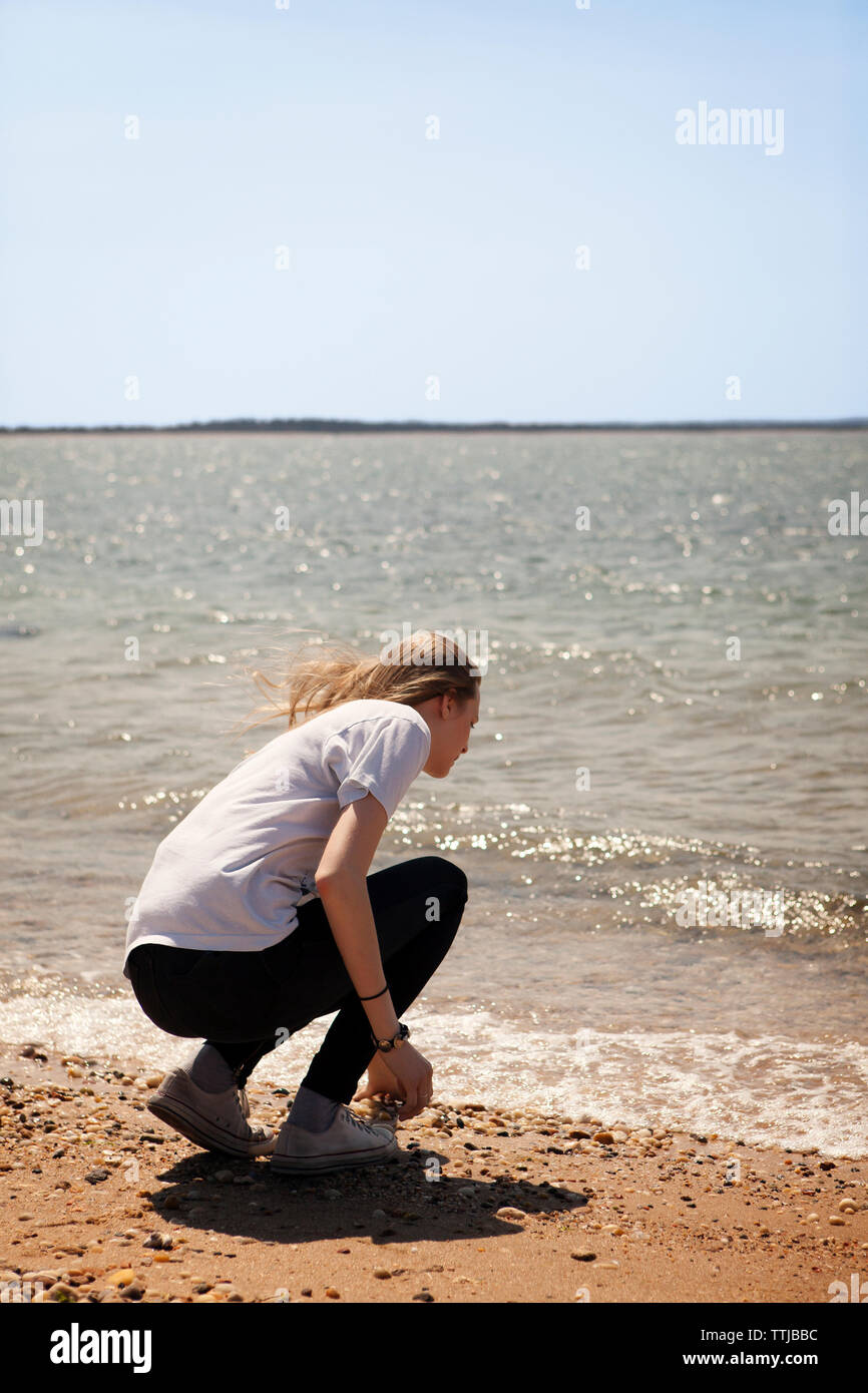 Rear view of woman crouching on shore at beach Stock Photo - Alamy