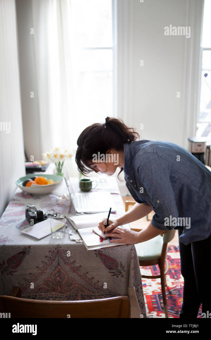 Side view of woman writing while standing by table at home Stock Photo