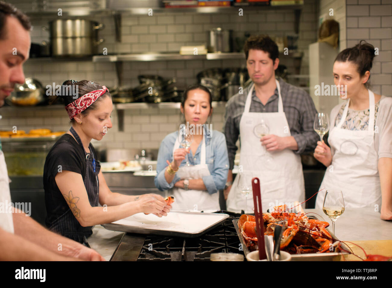 Students looking at female chef preparing food at commercial kitchen Stock Photo