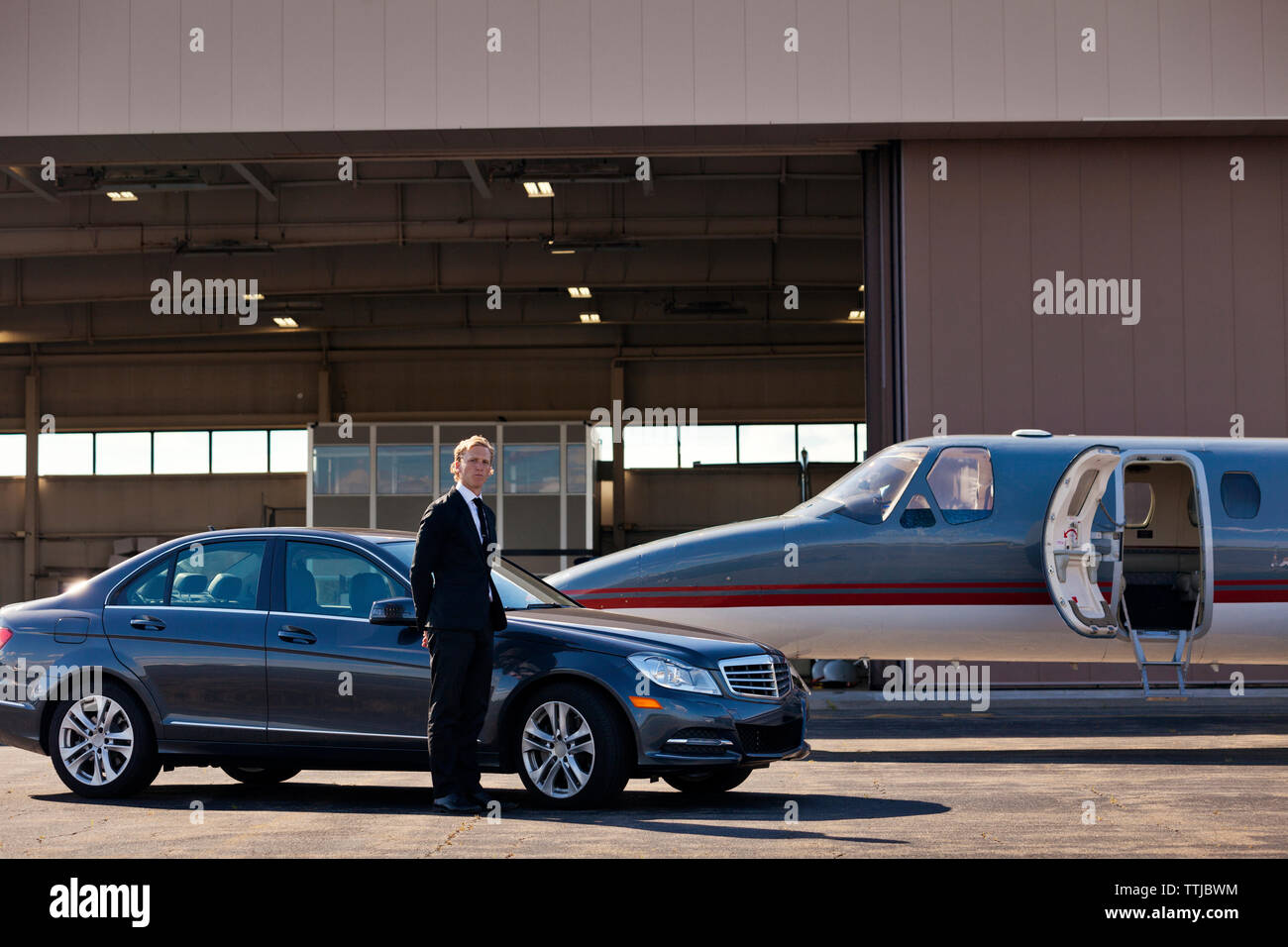 Portrait of businessman standing by car and airplane at airfield Stock Photo