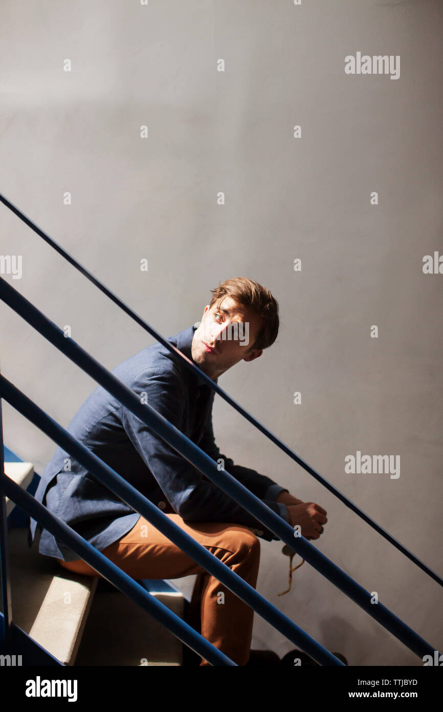 Man looking away while sitting on staircase Stock Photo - Alamy