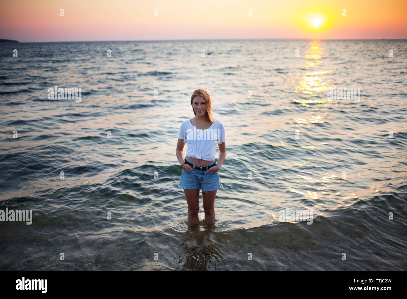 Portrait of woman with hands in pockets standing in water at beach ...