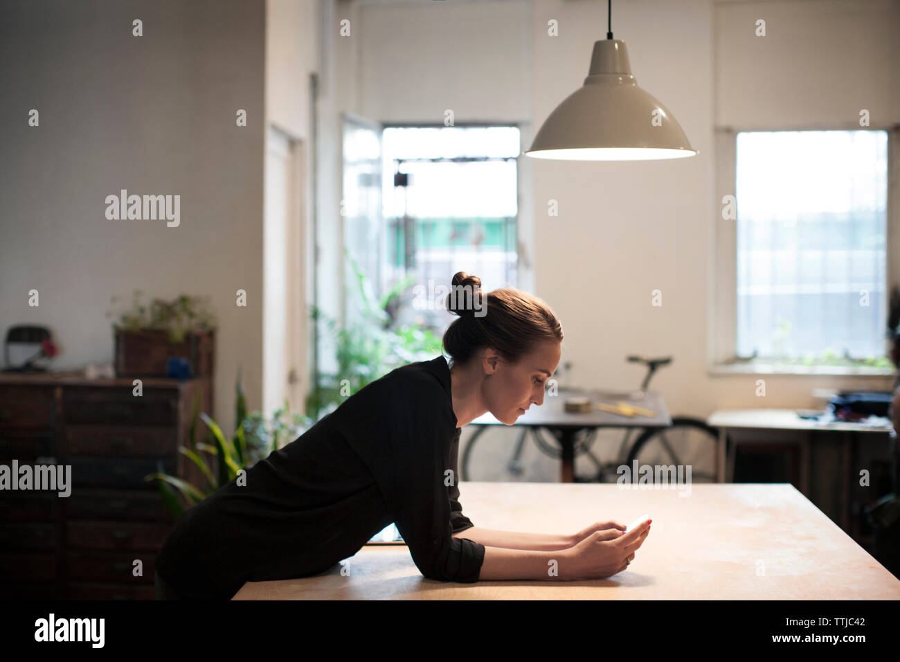 Side view of woman using smart phone while leaning on table Stock