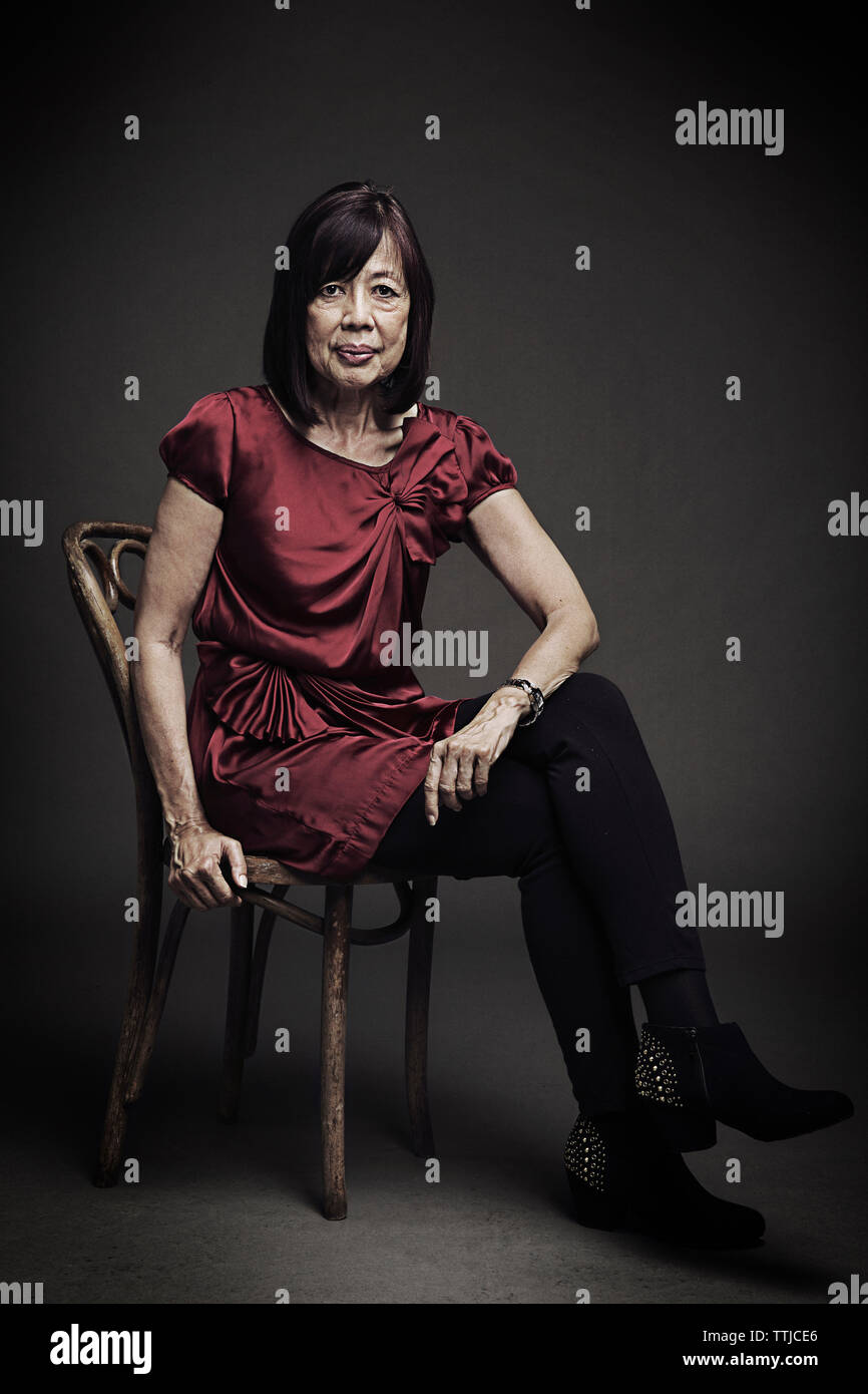Portrait of senior woman sitting on chair against black background ...