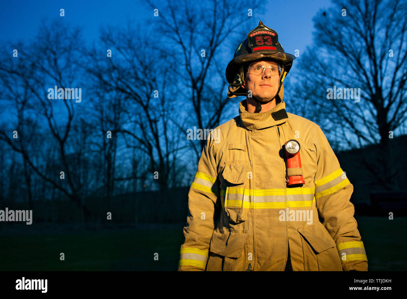 Firefighter looking away while standing against trees at night Stock Photo