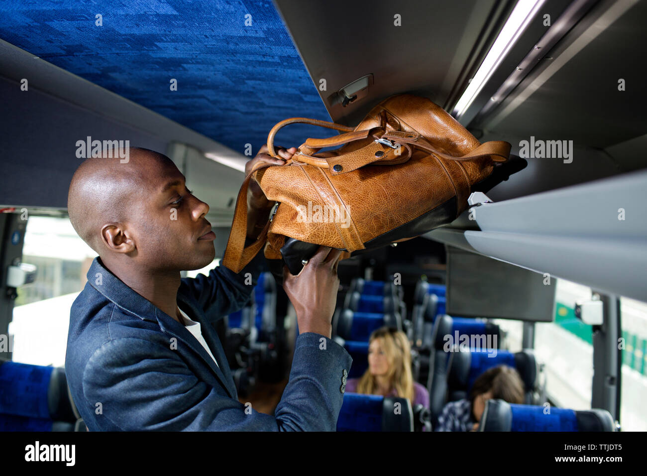 Man putting bag in luggage rack in bus Stock Photo