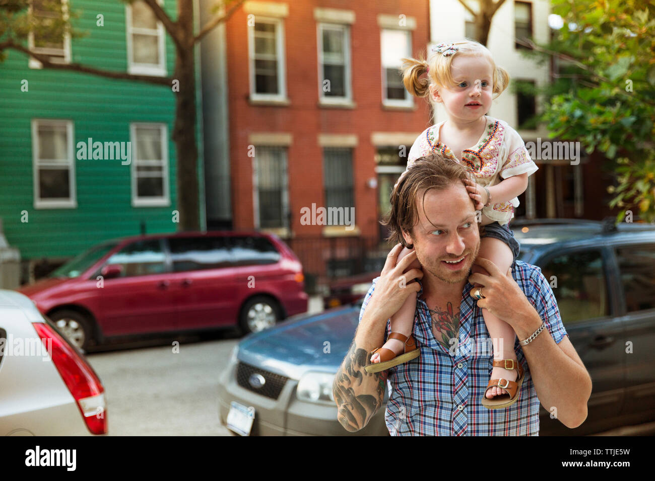 Father looking away while carrying baby girl on shoulder at city street Stock Photo