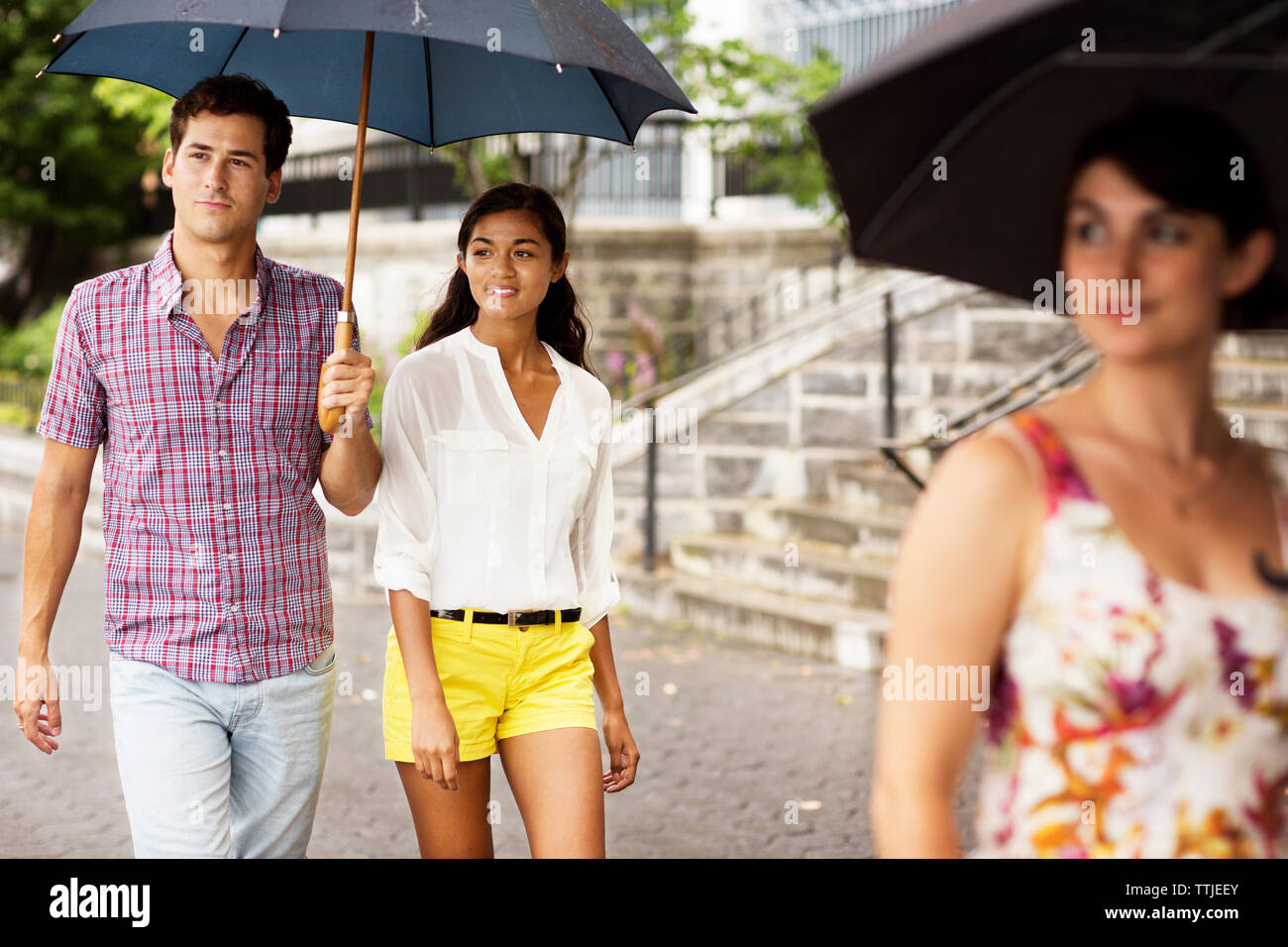Friends carrying umbrella while walking on footpath in city Stock Photo
