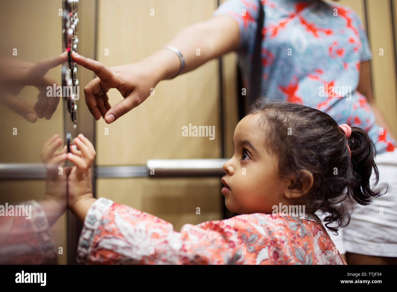 Woman pressing push button while daughter looking in elevator Stock Photo