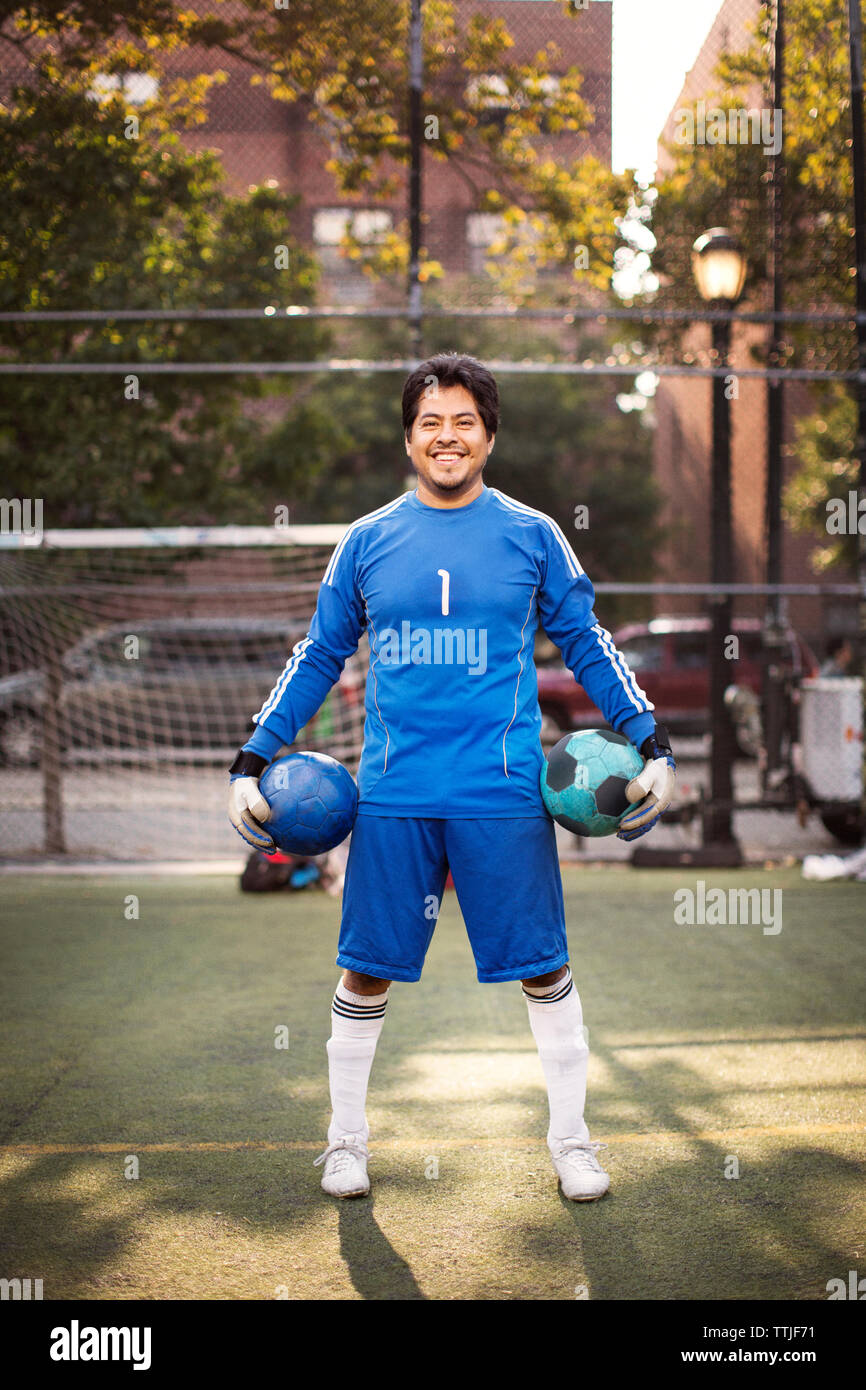 Portrait of happy soccer player carrying balls while standing at field Stock Photo