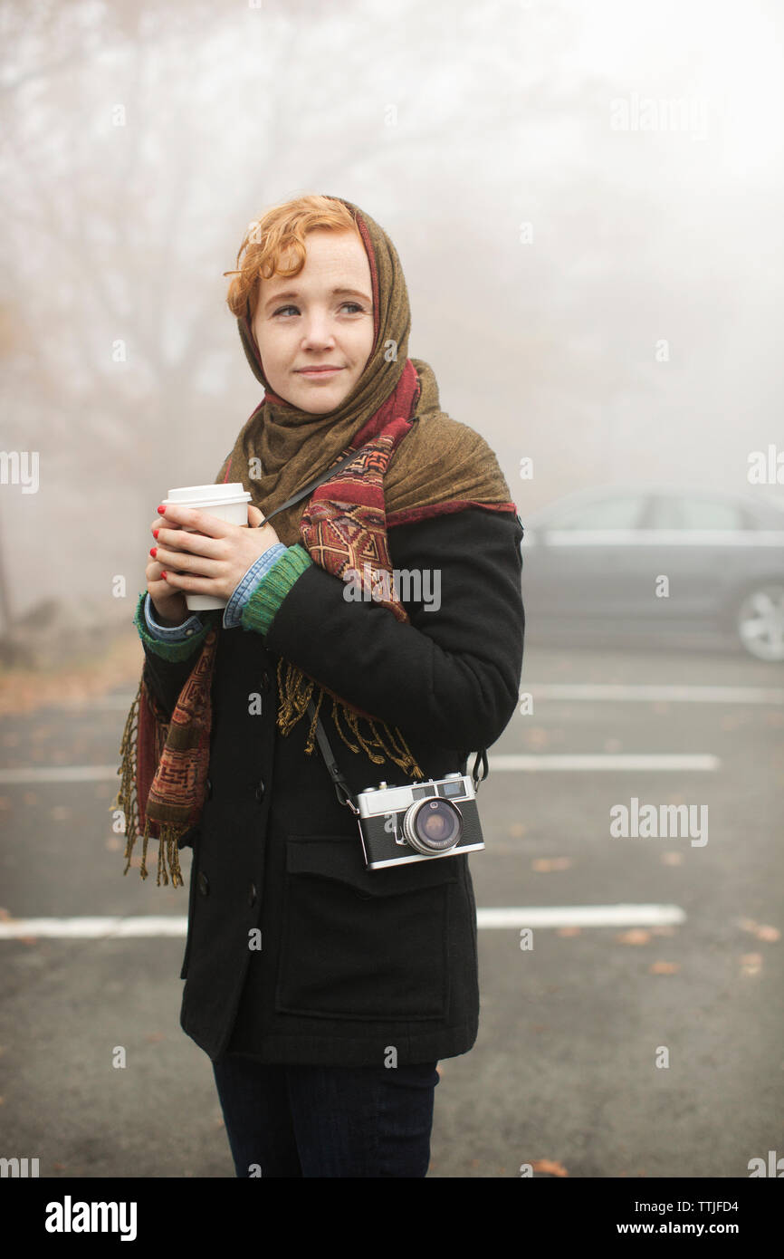 Woman with disposable cup looking away while standing on road in forest Stock Photo