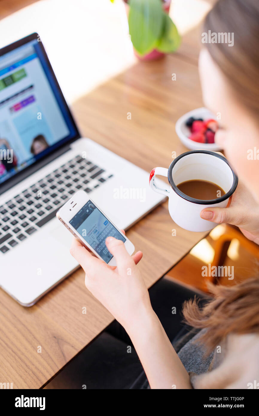 High angle view of woman using smart phone while drinking coffee at home Stock Photo