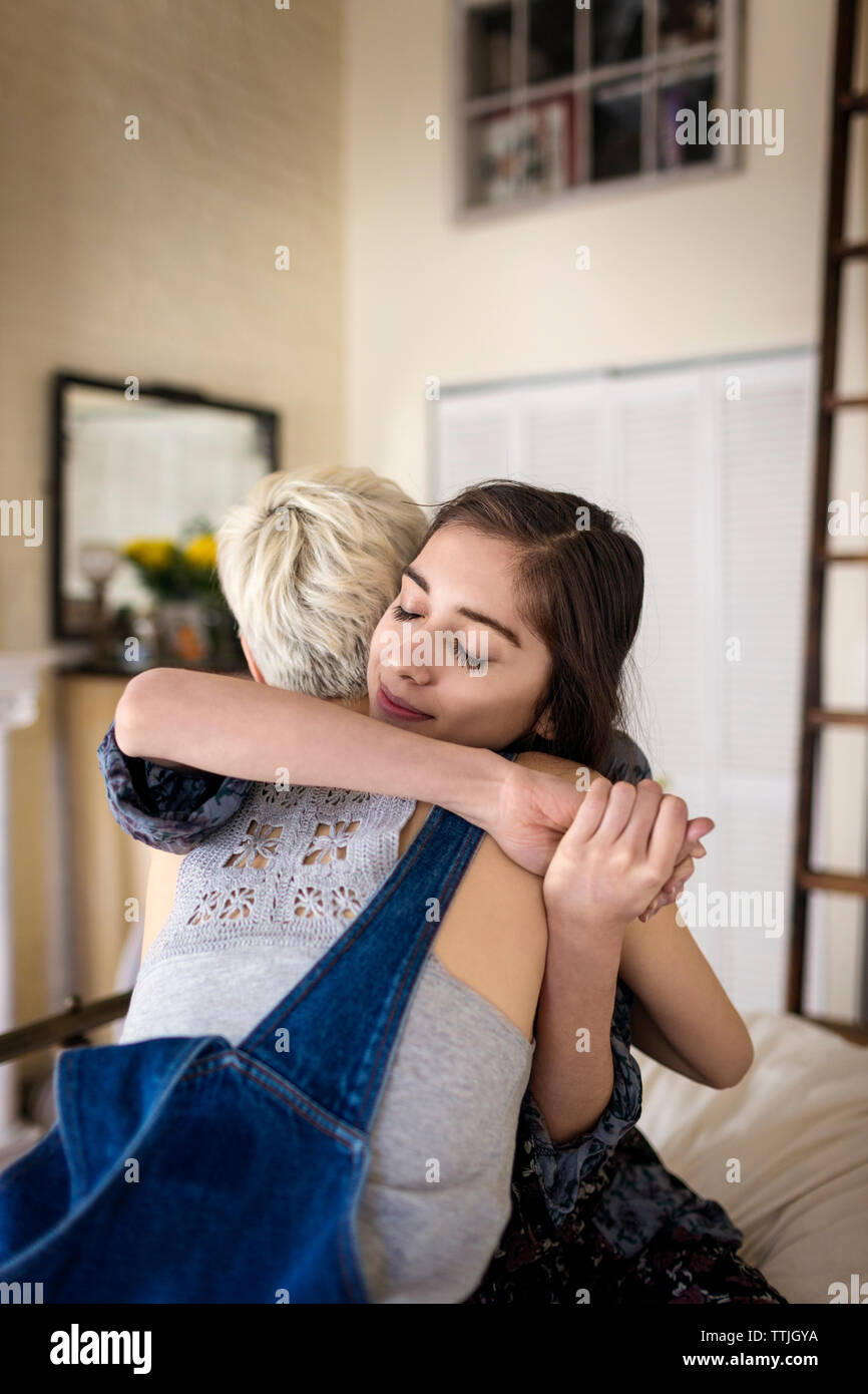 Female friends embracing while sitting on bed at home Stock Photo
