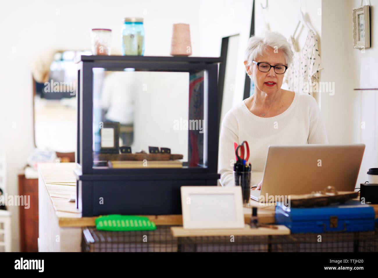 Senior woman using laptop computer in boutique store Stock Photo