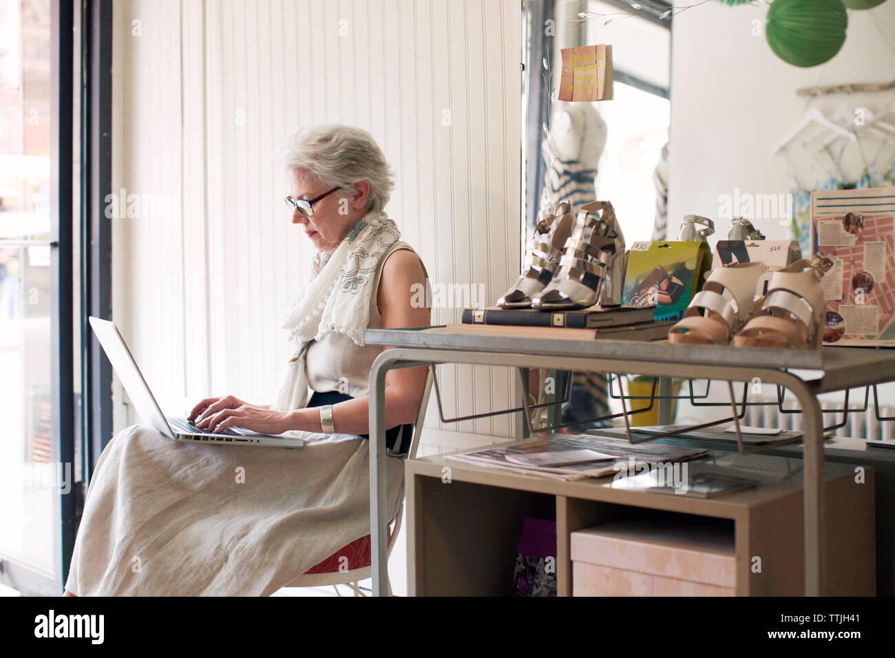 Side view of senior woman using laptop computer while sitting on chair in store Stock Photo